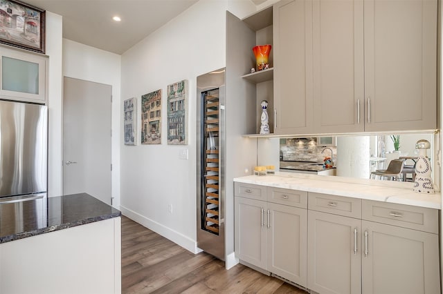 kitchen featuring light stone counters, stainless steel refrigerator, light wood-type flooring, and backsplash