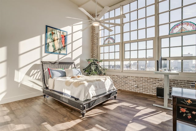 bedroom with wood-type flooring, a high ceiling, ceiling fan, and brick wall