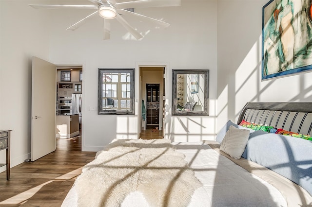 bedroom featuring ceiling fan, stainless steel fridge, a high ceiling, ensuite bath, and dark hardwood / wood-style flooring