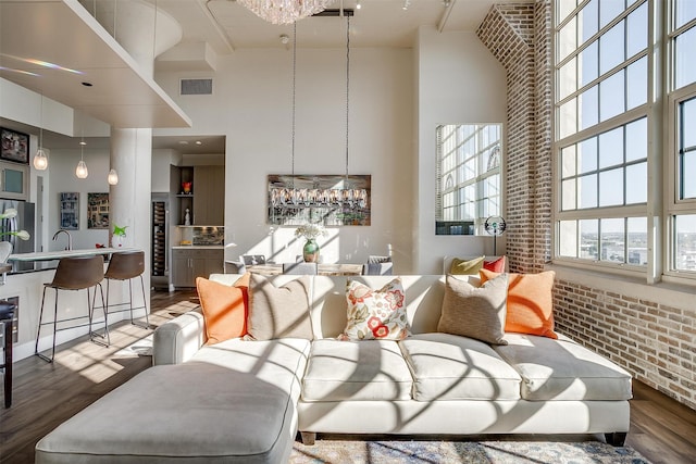 living room featuring wet bar, hardwood / wood-style floors, a towering ceiling, and brick wall