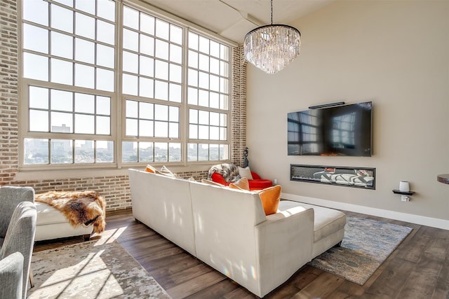 living room featuring a high ceiling, dark hardwood / wood-style flooring, a chandelier, and brick wall