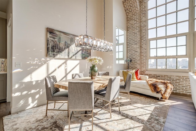 dining space featuring brick wall, hardwood / wood-style flooring, a towering ceiling, and a chandelier