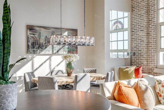 dining area featuring a notable chandelier, a towering ceiling, brick wall, and a healthy amount of sunlight