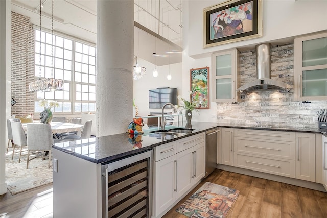 kitchen featuring decorative light fixtures, beverage cooler, wall chimney range hood, and white cabinets