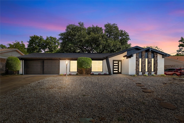 mid-century inspired home with a garage, stone siding, french doors, concrete driveway, and stucco siding