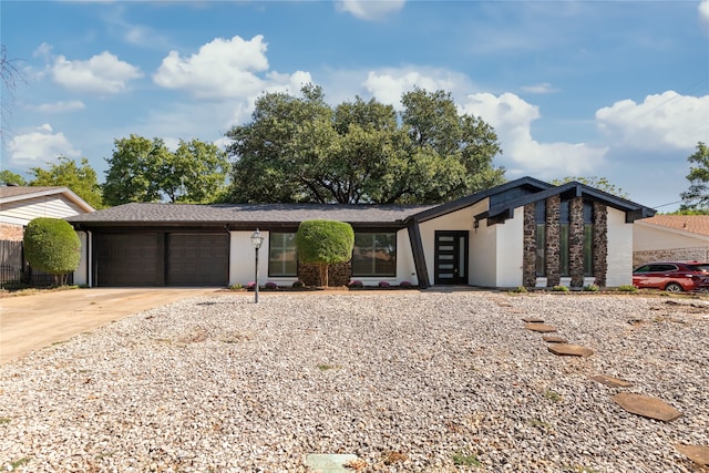 mid-century inspired home featuring driveway, stone siding, and a garage