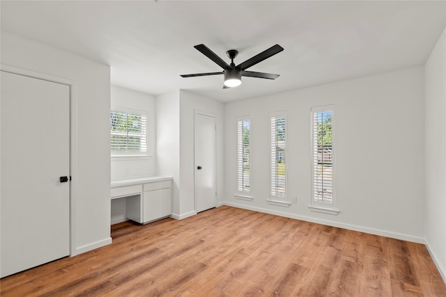 unfurnished bedroom with built in desk, light hardwood / wood-style floors, and ceiling fan