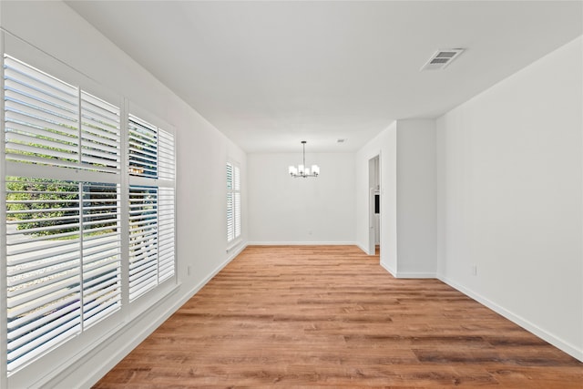 spare room with light wood-type flooring, visible vents, a notable chandelier, and baseboards