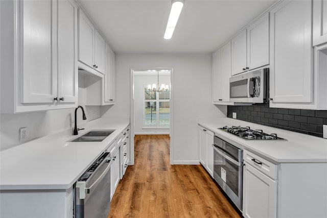 kitchen featuring light wood-style flooring, a sink, stainless steel appliances, white cabinetry, and backsplash