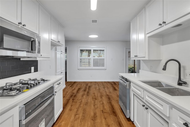 kitchen with stainless steel appliances, a sink, visible vents, white cabinets, and light countertops