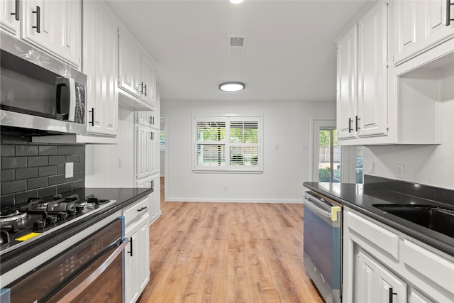 kitchen featuring decorative backsplash, stainless steel appliances, white cabinetry, and light wood-type flooring