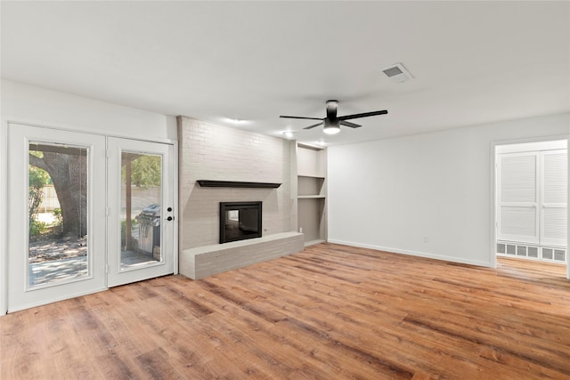 unfurnished living room with visible vents, baseboards, ceiling fan, wood finished floors, and a brick fireplace