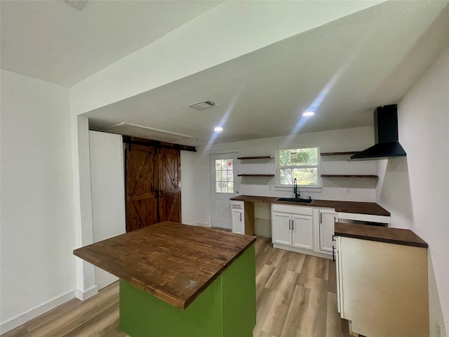 kitchen with wooden counters, light hardwood / wood-style flooring, white cabinetry, range hood, and a barn door