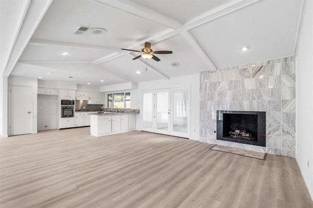 unfurnished living room featuring ceiling fan, light hardwood / wood-style flooring, tile walls, a fireplace, and vaulted ceiling with beams