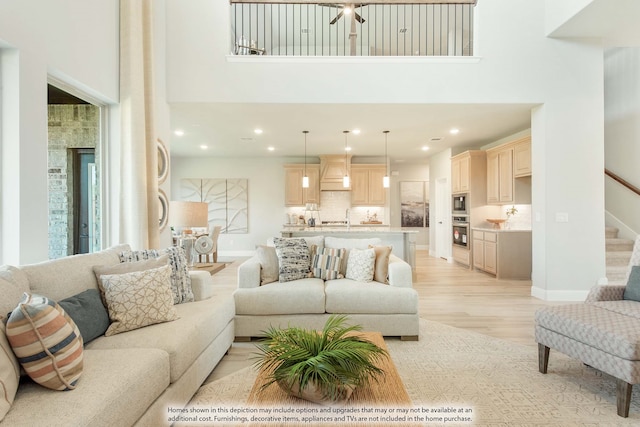 living room featuring light wood-type flooring, a towering ceiling, ceiling fan, and sink