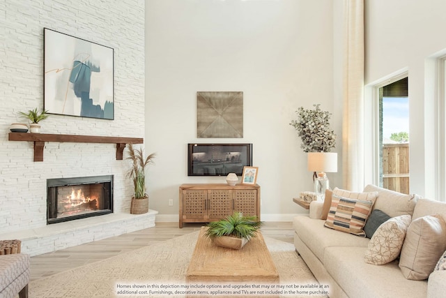 living room with a high ceiling, light hardwood / wood-style floors, and a stone fireplace