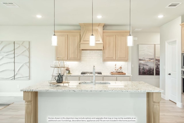 kitchen with light hardwood / wood-style floors, hanging light fixtures, and a kitchen island with sink