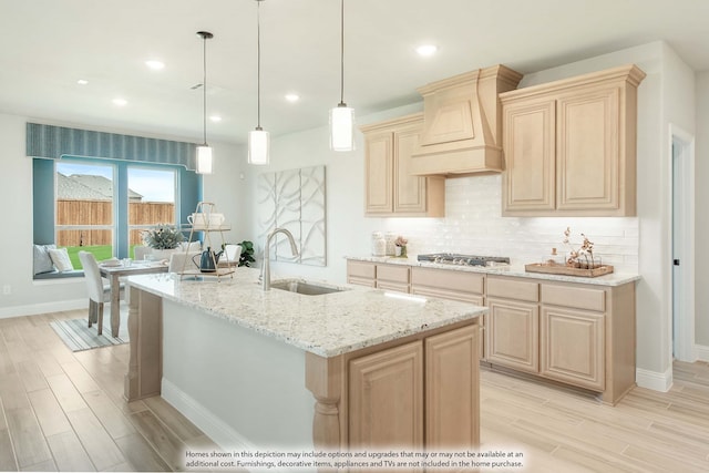 kitchen featuring sink, custom exhaust hood, a center island with sink, light brown cabinets, and decorative light fixtures