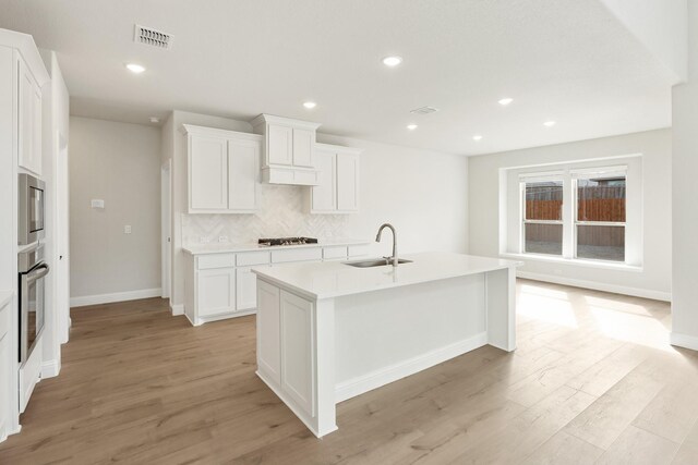 kitchen with dishwasher, a kitchen island with sink, sink, light brown cabinets, and a stone fireplace