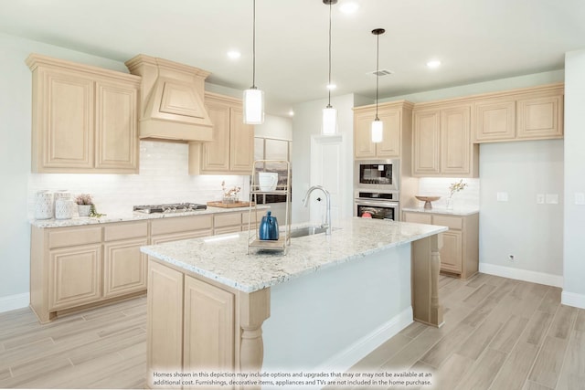 kitchen featuring appliances with stainless steel finishes, light hardwood / wood-style floors, light stone counters, a kitchen island with sink, and sink