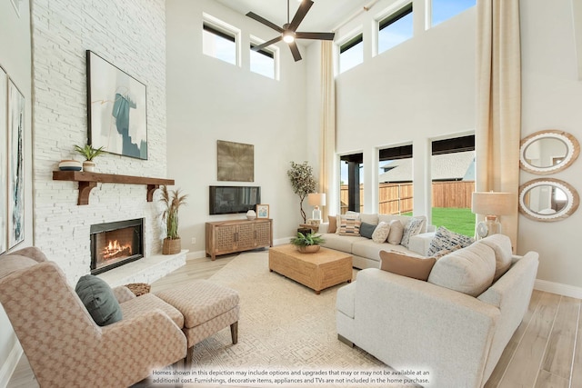 living room with light wood-type flooring, a fireplace, a towering ceiling, and ceiling fan