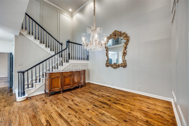 foyer entrance featuring hardwood / wood-style floors, a towering ceiling, ornamental molding, and an inviting chandelier