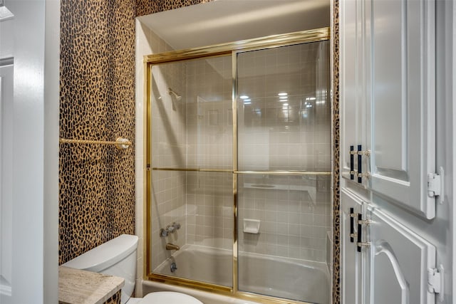 bathroom featuring toilet and bath / shower combo with glass door