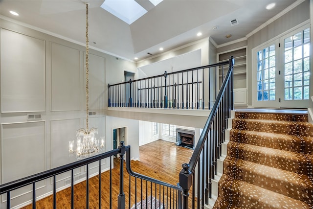 stairs with a chandelier, hardwood / wood-style flooring, a skylight, and crown molding