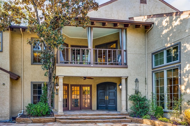 view of exterior entry with ceiling fan and a balcony