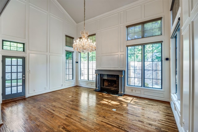 unfurnished living room with hardwood / wood-style floors, high vaulted ceiling, a high end fireplace, ornamental molding, and a notable chandelier