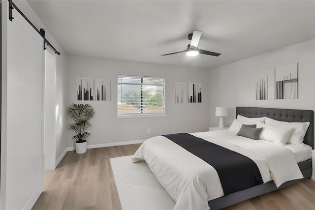 bedroom with ceiling fan, light hardwood / wood-style floors, and a barn door