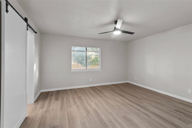 empty room featuring a barn door, light hardwood / wood-style flooring, and ceiling fan