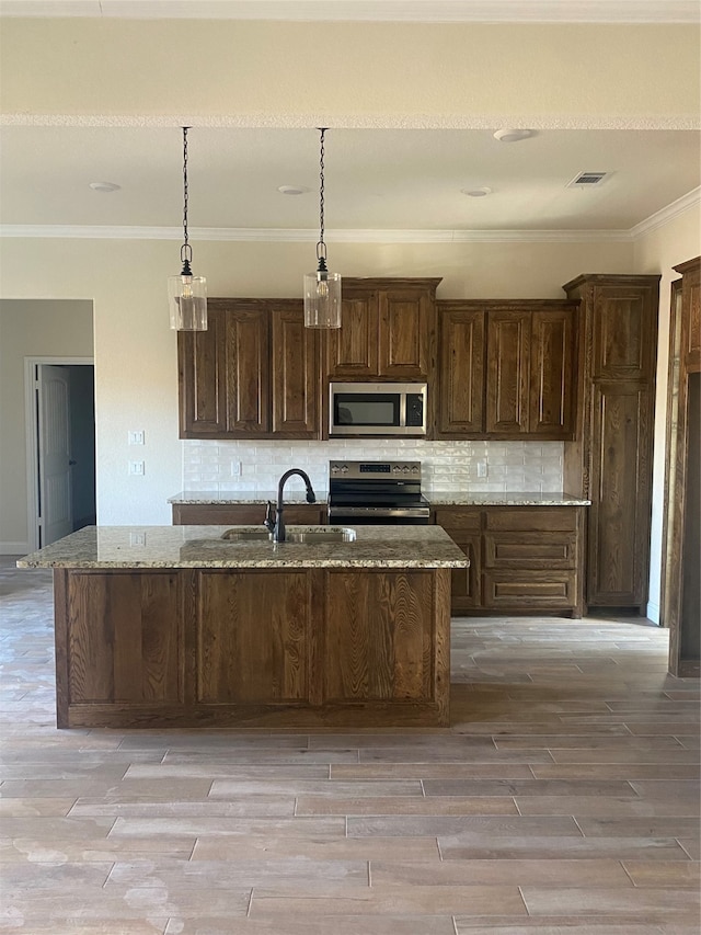 kitchen with appliances with stainless steel finishes, an island with sink, light stone counters, light hardwood / wood-style flooring, and dark brown cabinetry