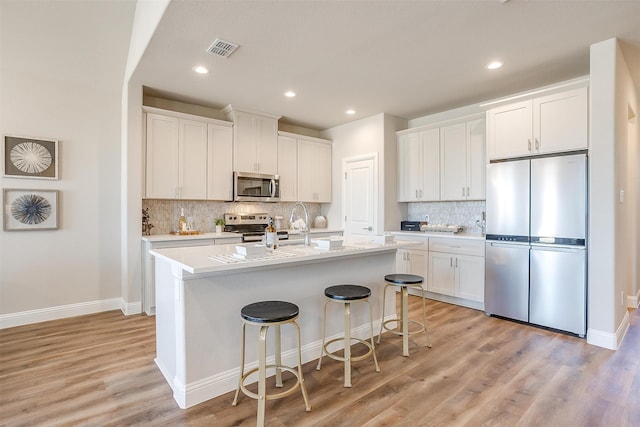 kitchen with white cabinets, a kitchen island with sink, appliances with stainless steel finishes, and light hardwood / wood-style floors