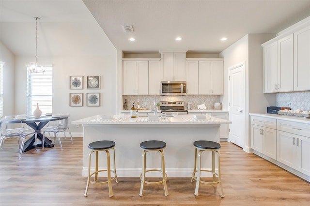 kitchen with light hardwood / wood-style flooring, a center island with sink, stainless steel appliances, and white cabinetry