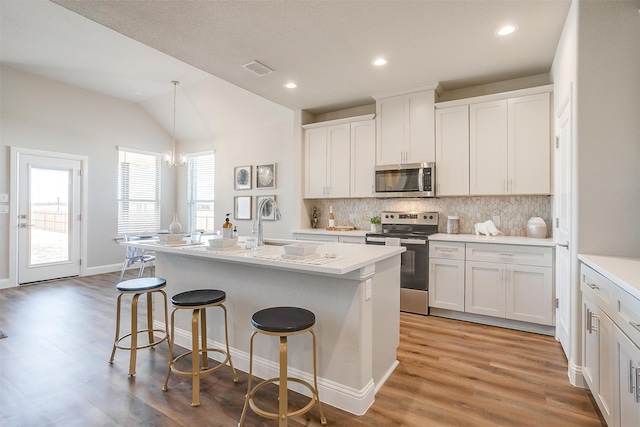 kitchen with white cabinets, lofted ceiling, a kitchen island with sink, appliances with stainless steel finishes, and light wood-type flooring