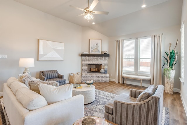 living room with ceiling fan, light wood-type flooring, a fireplace, and vaulted ceiling