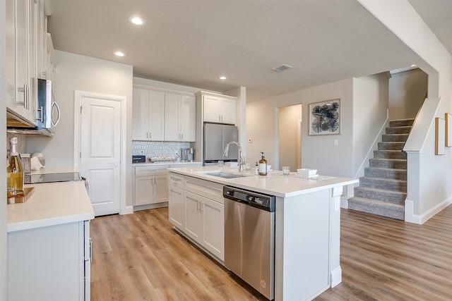 kitchen with white cabinets, an island with sink, sink, stainless steel appliances, and light hardwood / wood-style floors