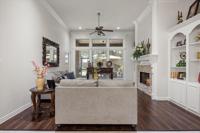 living room with a stone fireplace, crown molding, ceiling fan, dark hardwood / wood-style floors, and built in features