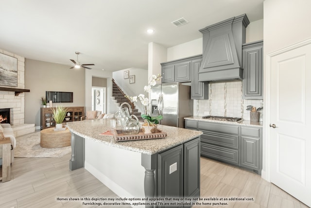 kitchen featuring premium range hood, an island with sink, gray cabinets, stainless steel appliances, and light stone countertops