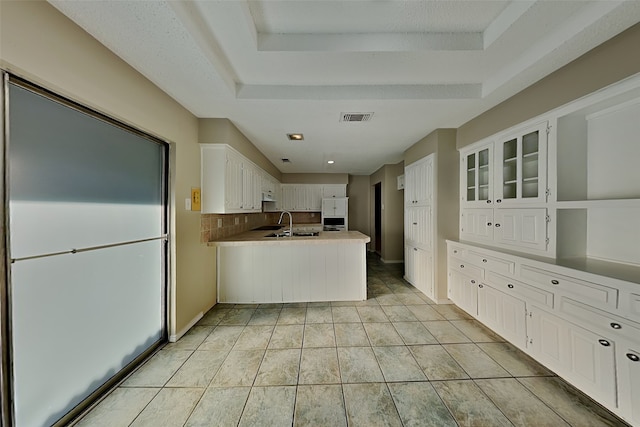 kitchen with a tray ceiling, white cabinetry, kitchen peninsula, backsplash, and light tile patterned floors