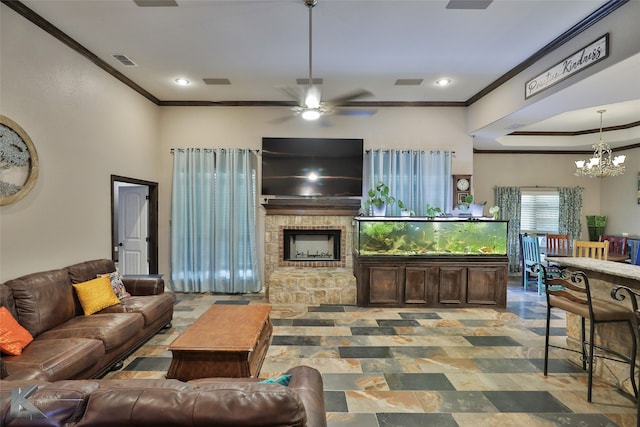 living room with a stone fireplace, ceiling fan with notable chandelier, and crown molding