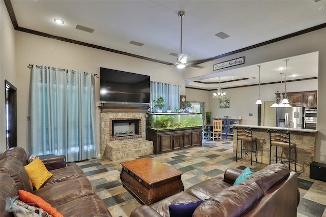 living room with ceiling fan with notable chandelier, ornamental molding, and a stone fireplace