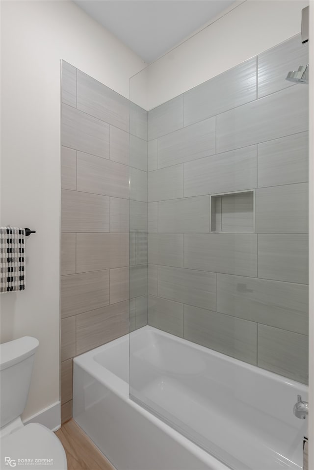 bathroom with hardwood / wood-style floors, toilet, and tiled shower / bath