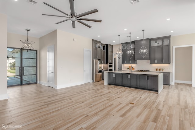 kitchen with pendant lighting, stainless steel appliances, light hardwood / wood-style flooring, and a kitchen island with sink