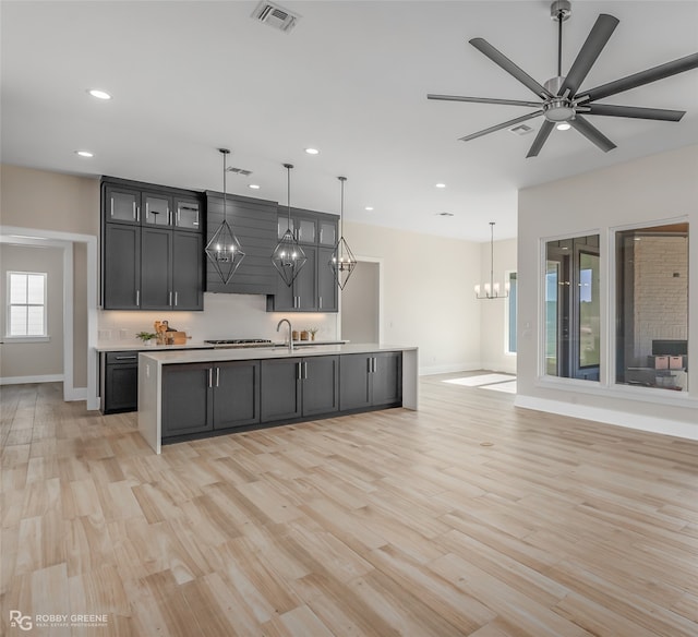 kitchen featuring ceiling fan with notable chandelier, a center island with sink, decorative light fixtures, and light hardwood / wood-style flooring