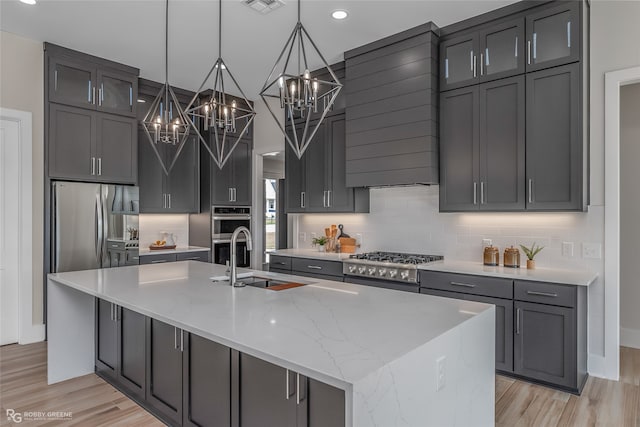 kitchen featuring appliances with stainless steel finishes, hanging light fixtures, light stone countertops, light wood-type flooring, and a spacious island