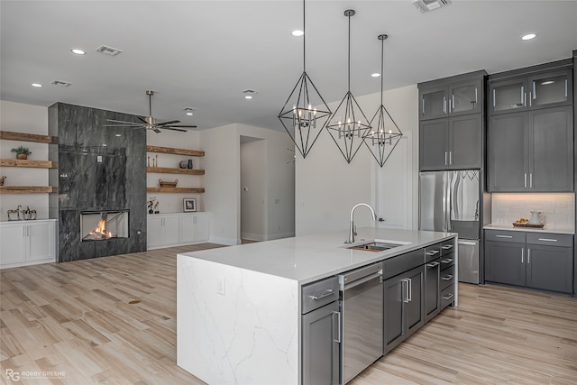 kitchen featuring appliances with stainless steel finishes, an island with sink, a high end fireplace, light hardwood / wood-style flooring, and sink