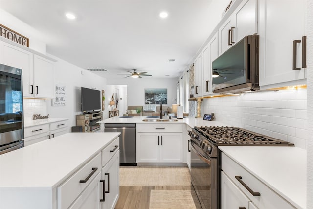 kitchen featuring kitchen peninsula, appliances with stainless steel finishes, light wood-type flooring, sink, and white cabinetry