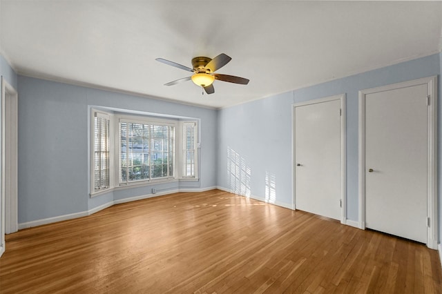 unfurnished bedroom with wood-type flooring, ceiling fan, and multiple closets